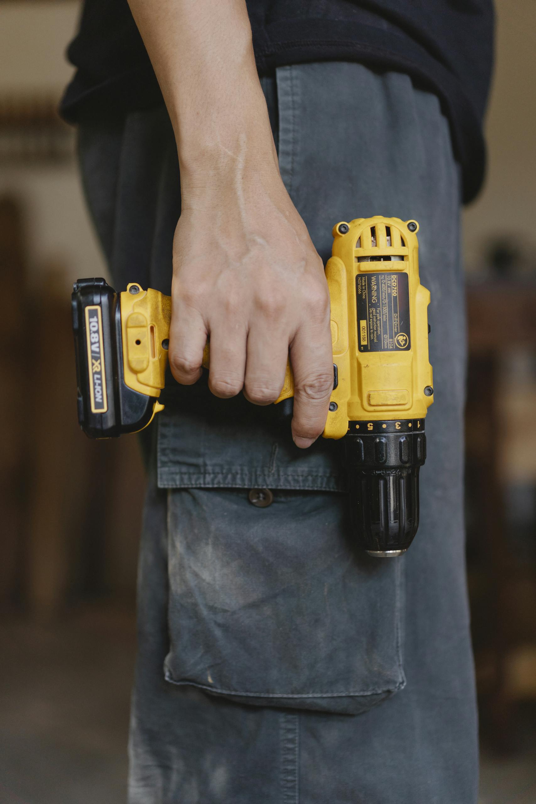 Side view of unrecognizable craftsman in casual clothes standing with electric cordless screwdriver in workshop